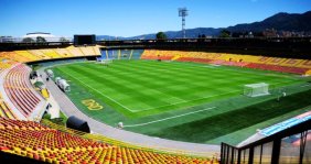 Vista panorámica de un estadio con gradas rojas y amarillas y césped verde en el medio
