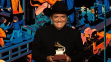 Un hombre con traje negro llanero, sombrero y un grammy en las manos