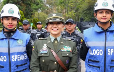 Mujer vestida de policía en el centro con dos mujeres con chalecos azules y cascos blancos a los lados